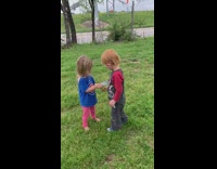 Two blonde kids phone grass hand flowers