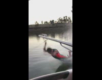 Boy water skis while holding onto boat, does the shaka sign and falls into water