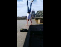 Guy handstands on wall edge near river  