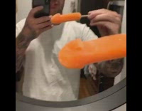 Guy holds orange popsicle looks like penis 