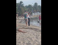 Woman dances while man films at beach