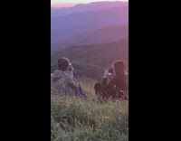 Couple hold camera sit grass mountain sunset